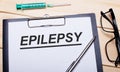 The word EPILEPSY is written on a white piece of paper next to black-rimmed glasses, a pen and a syringe. Medical concept Royalty Free Stock Photo