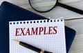 The word EXAMPLES on a white sheet of paper against the background of a fragment of a notebook and a pen Royalty Free Stock Photo