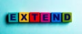 The word EXTEND is written on multicolored bright wooden cubes on a light blue background