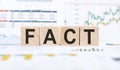 Word FACT made with wood building blocks on background from financial graphs and charts Royalty Free Stock Photo