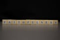 The word FAITHFULNESS written on wooden cubes isolated on a black background