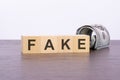 the word FAKE on wood cubes and banknotes on the background, business and finance concept Royalty Free Stock Photo
