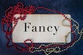 The word fancy painted on wooden board with red and gold beaded necklaces flat lay