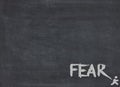 The word fear in chalk on blackboard with little man running away