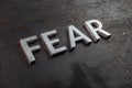 The word fear laid with silver letters on raw rusted steel sheet surface in diagonal slanted perspective