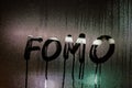 word FOMO - Fear Of Missing Out - handwritten on night wet window glass surface