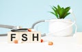 The word FSH is written on wooden cubes near a stethoscope on a wooden background. Medical concept Royalty Free Stock Photo