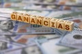 The word `Ganancias` in Spanish which means Profits, text written on wooden blocks with American banknotes