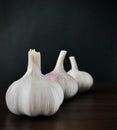 Three garlics on wood brown table, black background. Square.