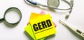 The word GERD is written on a yellow sticker next to the stethoscope, magnifying glass and electronic thermometer. Medical concept Royalty Free Stock Photo
