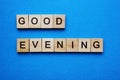 The word Good Evening, written in printed wooden letters on a blue background. A wish, a greeting.