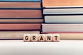 The word grant on wooden cubes with stacked books background. Education or research funding concept