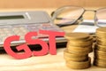 The word GST from paper letters and coins and a calculator on a natural wooden table. Taxes Royalty Free Stock Photo