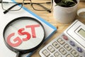 The word GST from paper letters and a magnifying glass and a calculator on a natural wooden table. Taxes Royalty Free Stock Photo