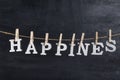 Word HAPPINES held on a clothespin on a rope against black background. Inscription from white letters