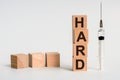 The word HARD formed by wooden blocks on a white table. Next to it is a syringe - a threat to life, a medical concept Royalty Free Stock Photo