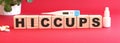 The word HICCUPS is made of wooden cubes on a red background. Medical concept