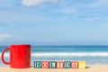 word HOLIDAY in colorful alphabet blocks and coffee cup on tropical beach