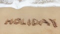 Word HOLIDAY written on wet sand of beach, small spot of white sea water in top part