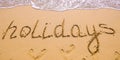 Word Holidays hand written in the sand with a sea wave. Close up sand texture on beach in summer Royalty Free Stock Photo