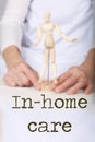 Word IN-HOME CARE. Wooden figurine in the hands of an old woman in the background