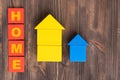 The word HOME on red wooden cubes. Large yellow and small blue house made of wooden cubes on a brown wooden background, top view