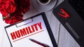 The word HUMILITY is written in red on a white notepad near a laptop, coffee, red roses and a pen Royalty Free Stock Photo