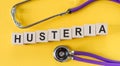 The word hysteria made from wooden cubes on a yellow table with a stethoscope. Medical concept
