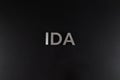 the word ida laid with silver metal letters over dry black matte surface