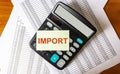 The word IMPORT on a white sticker on a calculator and papers on a wooden table Royalty Free Stock Photo