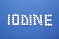 Word Iodine made of pills on blue background, flat lay