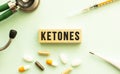 The word KETONES on a wooden cube with a stethoscope and pills. Medical concept. Flat lay.