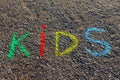Word KIDS written with colorful crayons on the asphalt, ground.