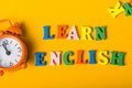 Word LEARN ENGLISH made with wooden letters on orange desk litle clock. Concept of English language courses