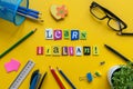 Word LEARN ITALIAN made with carved letters onyellow desk with office or school supplies, stationery. Concept of Italian
