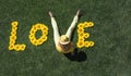 Word love, laid out from sunflower flowers on green lawn. Instead of letter V - girl`s legs in yellow pants