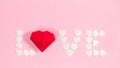 Word Love is lined with small white hearts and a large red origami heart. Pink background. Greeting card