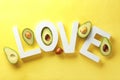 Word LOVE made of letters and halves of ripe avocados on color background