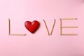 Word LOVE made of pencils and decorative heart on pink background, flat