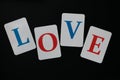 The word love made up of letters of blue and red color on white cards laid out on a black background