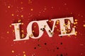 The word Love sprinkled with shiny confetti on a red background. Bright backdrop with silver and gold round glitters Royalty Free Stock Photo