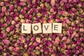 The word love on wooden tiles among many dried aromatic rose buds