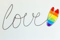 The word Love is written in black marker with a heart painted in the colors of the Lgbt flag rainbow heart shape on white. Concept