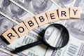 Word made of wooden letters - robbery, on a gray background with us dollars next to a magnifier. Crime investigation concept Royalty Free Stock Photo