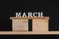 Word March written on wooden blocks on wooden shelf. Black background. Spring calendar