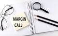 Word MARGIN CALL on the sicker on notebook with pencils,magnifier and glasses