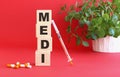 The word MEDI is made of wooden cubes on a red background. Medical concept