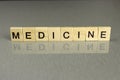 The word medicine, made of square wooden letters on a gray background