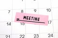 The word Meeting written on a pink sticky note posted on a calendar or planner page. Closeup of a personal agenda