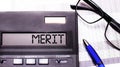 The word MERIT is written in the calculator near black-framed glasses and a blue pen Royalty Free Stock Photo